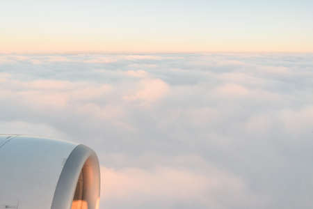 The view from the airplanes illuminator to the wing, airplane turbine and fluffy clouds at sunrise. Flying over the cloudsの写真素材