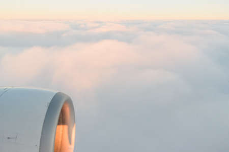 The view from the airplanes illuminator to the wing, airplane turbine and fluffy clouds at sunrise. Flying over the cloudsの写真素材