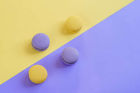 Sweet tasty violet and yellow french macaron cakes on yellow and violet background.の写真素材