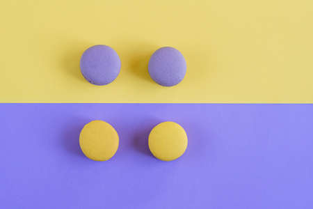 Sweet tasty violet and yellow french macaron cakes on yellow and violet background.の写真素材