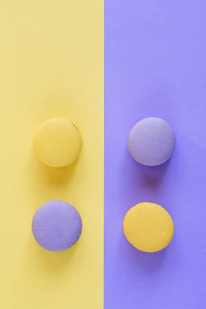 Sweet tasty violet and yellow french macaron cakes on yellow and violet background.の写真素材