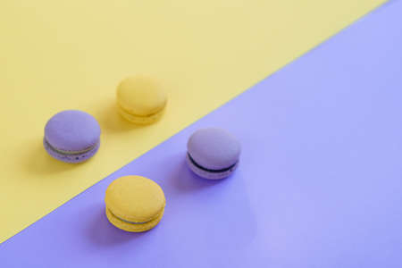 Sweet tasty violet and yellow french macaron cakes on yellow and violet background.の写真素材