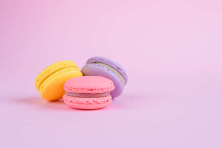 Tasty violet, pink and yellow french macaron cakes on pink background.の写真素材