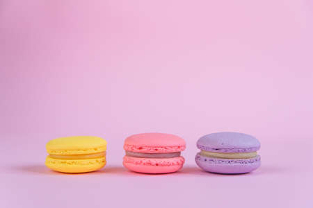 Tasty violet, pink and yellow french macaron cakes on pink background.の写真素材