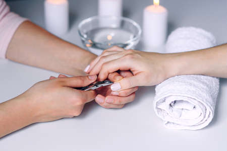 Nails beauty. Woman hands receiving nail care treatment by professional manicure specialist in nail salon. Manicurist cutting cuticle on nails with nail clippersの写真素材