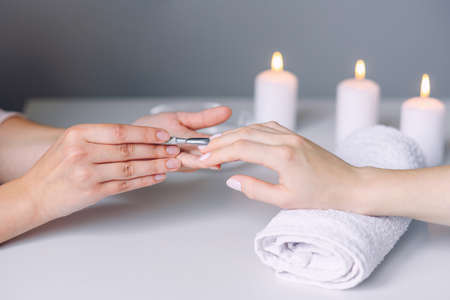Nail care. Closeup of beautiful woman hands getting manicure in spa salon. Female manicurist cleaning cuticle with professional manicure pusher tool.の写真素材