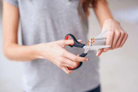 Quit smoking, health care concept. No smoking. Close up of female hands holding bunch of cigarettes and cutting them in halves with ccissors. Stop smoking concept.の写真素材