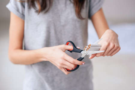Quit smoking, health care concept. No smoking. Close up of female hands holding bunch of cigarettes and cutting them in halves with ccissors. Stop smoking concept.の写真素材