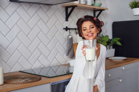 Smiling woman gives to the camera a glass of fresh milk in the stylish cozy kitchen at the morning.の写真素材