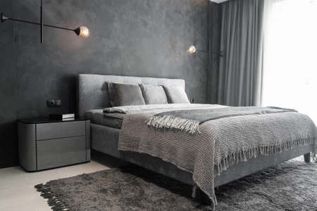 Master bedroom for a lonely stylish man, a bachelor. Modern room with trendy gray interiors, large king-size and lamps.の写真素材