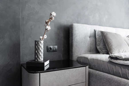 Stylish bedside table with dark book and vase with dried cotton branch on it. Interior details.の写真素材