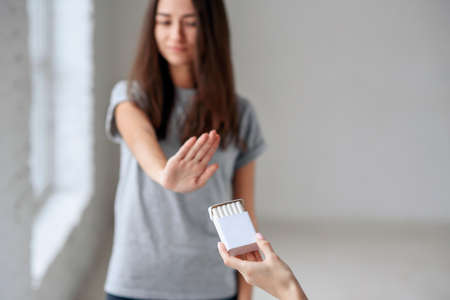 Healthy young beautiful girl refusing to take cigarette from package. Portrait of female showing stop sign with hand to cigarettes. Quit smoking, health care concept.の写真素材