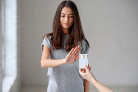 Healthy young beautiful girl refusing to take cigarette from package. Portrait of female showing stop sign with hand to cigarettes. Quit smoking, health care concept.の写真素材