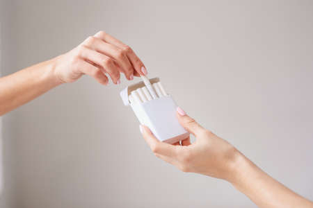 Close up of female hand holding cigarettes pack and proposing cigarette to another person. Close up of female hand taking cigarette from package.の写真素材