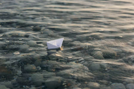 White paper boat floats on water with waves and ripples.の写真素材