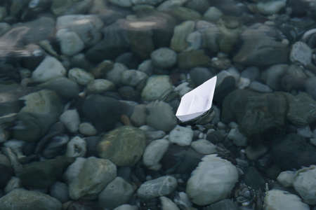 Alone paper boat floats in dark water at the stones background.の写真素材
