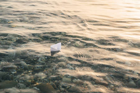 Paper boat floats on water with waves and ripples. Lonely toy boat at the sea.の写真素材