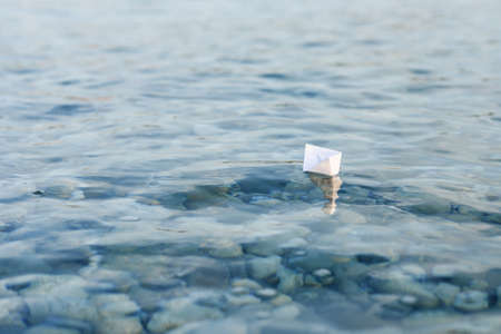 Origami paper boat sails on the surface of waterの写真素材