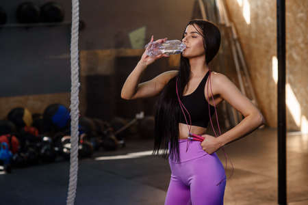 Beautiful fit woman drinking water from plastic bottle after workout in the gym.の写真素材
