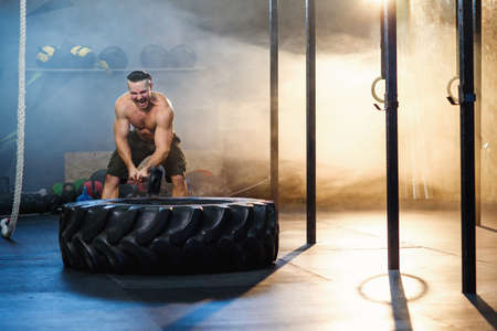 Strong young man hitting wheel tire using hammer in the gym.