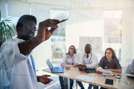 Young multiethnic interns listening lecture afro american doctor at medical conference in the clinic. During lecture the doctor writtig on board some formula for internes in the conference room atの写真素材