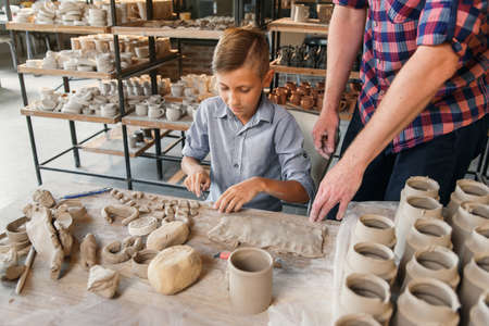 Middle age caucasian father teaching little son how to work with clay on potters wheel.の写真素材