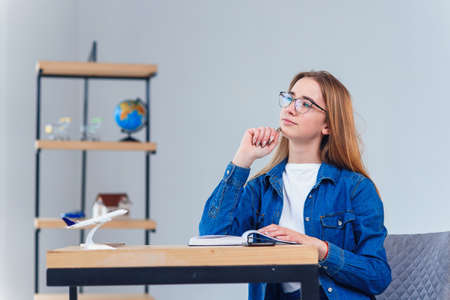 Young girl dreams about vacations while studying at white living room. Studying geography with...