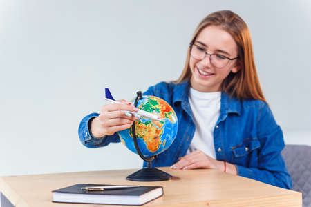 Young beautiful woman moving model of air plane around the globe and dreaming about future vacation abroad.の写真素材