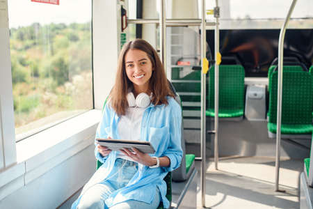 Happy smiling woman reads a tablet or ebook in a modern tram or subway. Pretty girl rides for work...