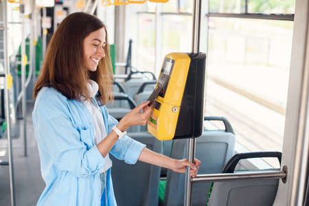 Female traveler pays contactless with bank card for the public transport in the tram or subway.