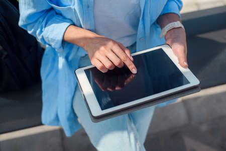 Female hand uses a tablet while waits on a public transport station.