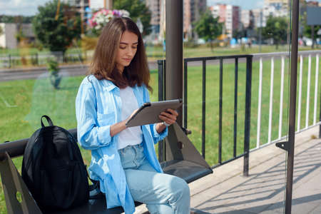 Happy woman uses a tablet or ebook on a tram station while waiting for public transport.の素材 [FY310130220544]