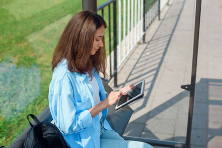 Happy woman uses a tablet or ebook on a tram station while waiting for public transport.