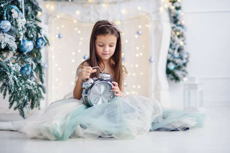 Cute girl with big clock in the hands sits near Christmas tree indoors.の写真素材