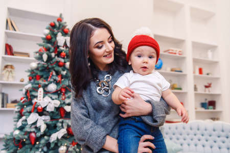 Happy beautiful mother having fun with her infant son near Christmas Tree in Christmas evening.の写真素材