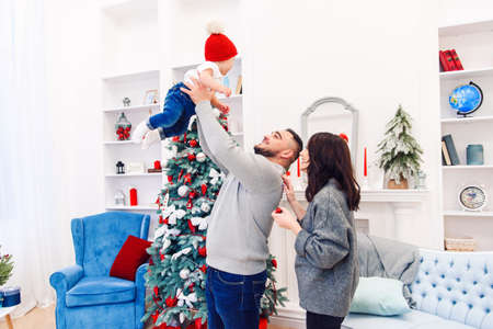 Attractive mommy stands near handsome gorgeous dad which throwing up their adorable little son in the air near festive decorated christmas tree.の写真素材