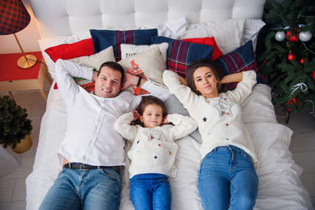 Merry Christmas and Happy New Year Happy family lying in bed near beautiful Christmas tree.の写真素材