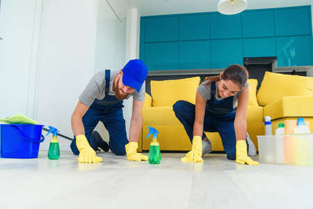 Smiling girl and handsome bearded man in workwears washing the parquet with the cleaning items and wipping with ragsの写真素材