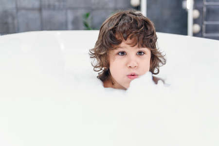 Funny little boy plays with foam in a bath.の写真素材
