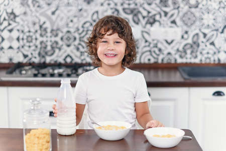 Happy boy feels happiness while eating healthy breakfast of cornflakes and milk at the kitchen.の写真素材