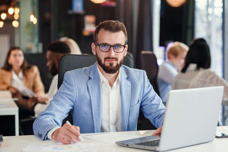Close up handsome confident bearded office manager in business suit works with laptop at the office room.の写真素材