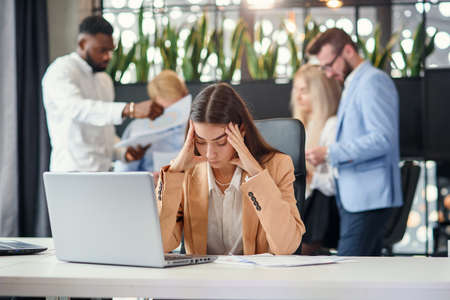 Young business woman working at office table in front of laptop suffering from headache feeling tired after hard workday.の写真素材
