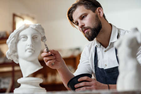 Skillful sculptor makes professional restauration of gypsum sculpture of womans head at the creative workshop.の写真素材
