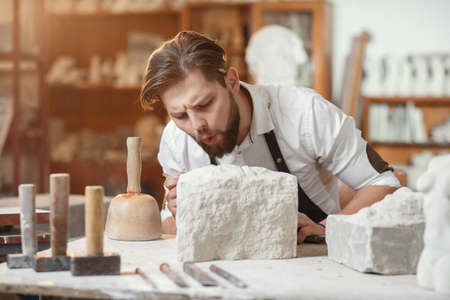 Handsome sculptor brushing stone head sculpture on the table in the atmospheric studioの写真素材