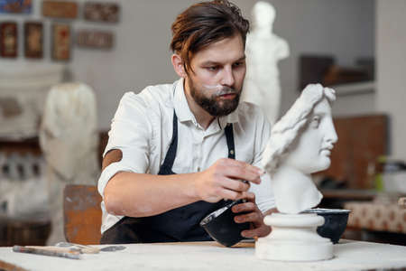 Skillful sculptor makes professional restauration of gypsum sculpture of womans head at the creative workshop.の写真素材