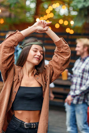 Beautiful girl dancing at foreground while her friends dancing in light of colored lamps during...