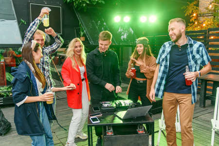 Group of friends drinking beer, dancing to the music, chatting and having a good rest time at...