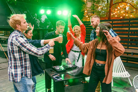 Group of friends drinking beer, dancing to the music, chatting and having a good rest time at...