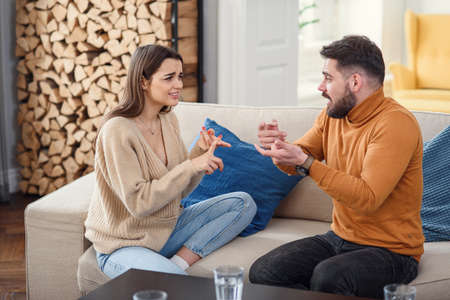Upset couple at home. Handsome man and beautiful young woman are having quarrel. Sitting on sofa...