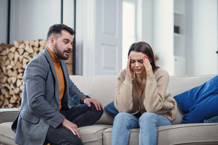 Upset couple at home. Handsome man and beautiful young woman are having quarrel. Sitting on sofa together. Family problems.の写真素材